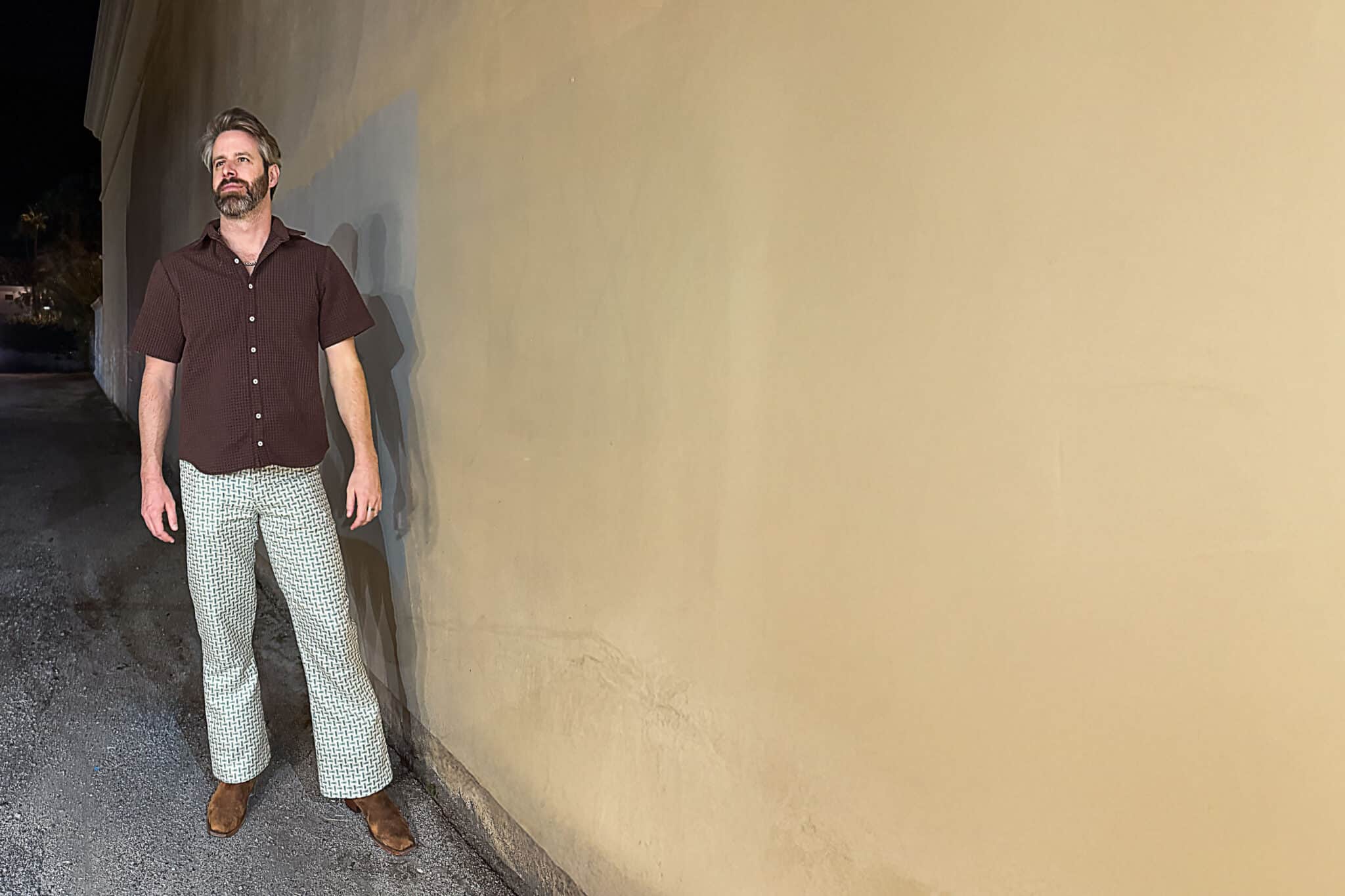 Man wearing casual shirt and patterned pants standing outdoors at night.