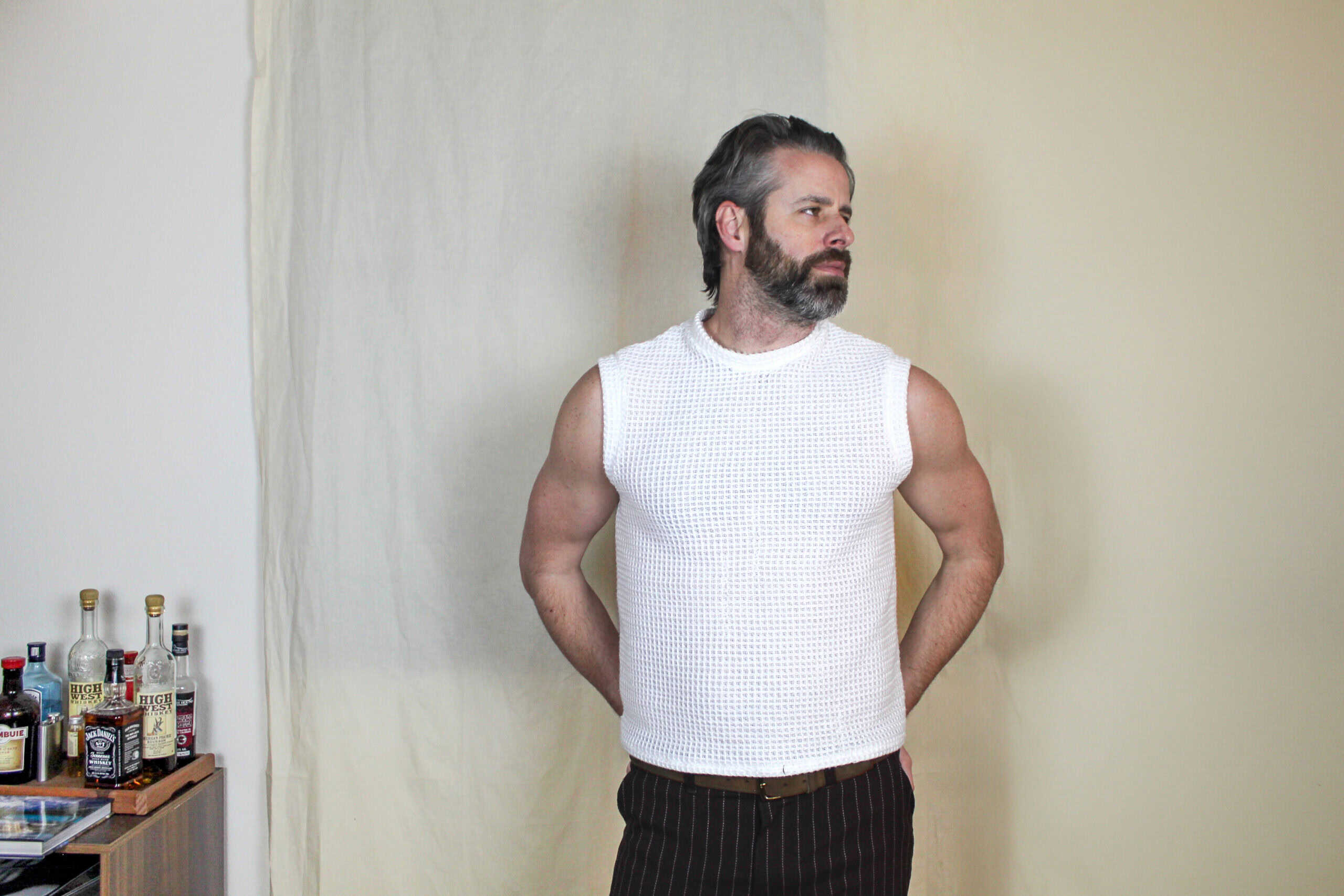 Male model wearing a white sleeveless knit top, standing against a plain background.
