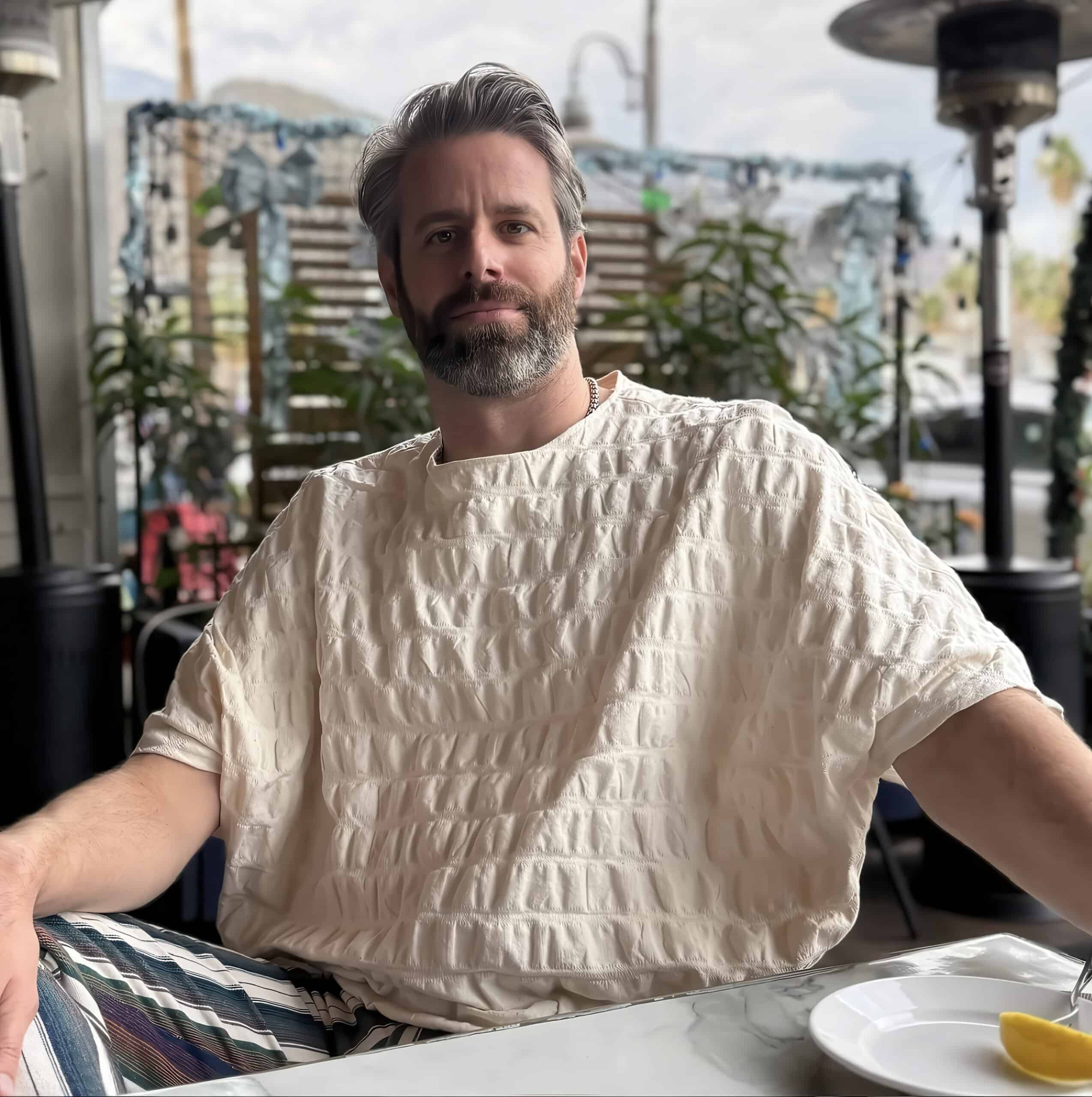 Man wearing a textured beige shirt at an outdoor cafe, enjoying a relaxed moment.