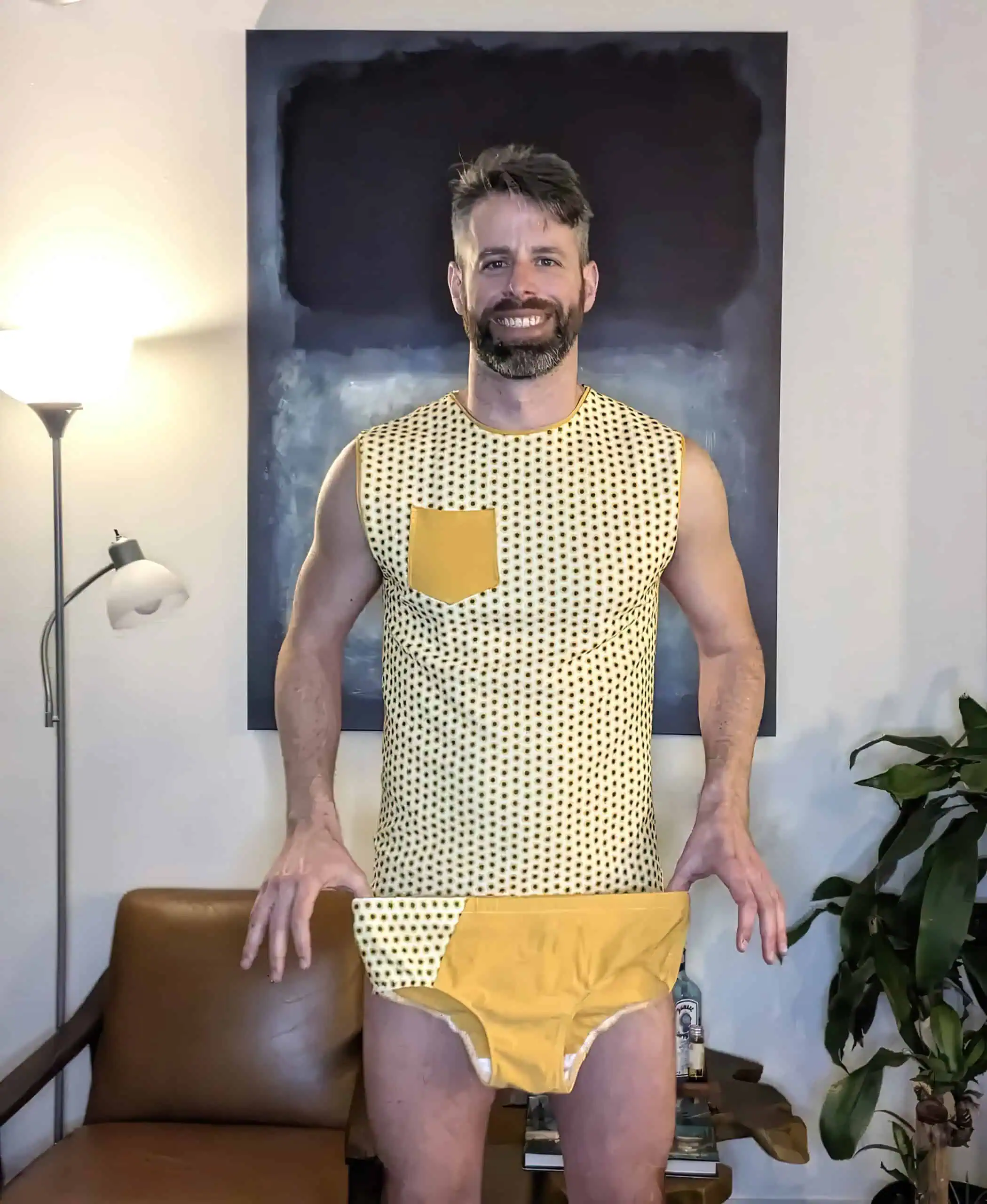 Man wearing a sleeveless yellow and black polka dot shirt with a yellow pocket, standing indoors.