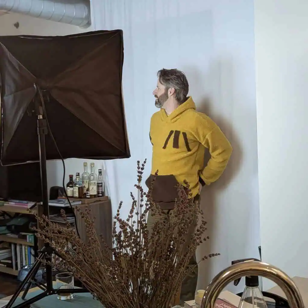 Man wearing a yellow fleece hoodie with a front pocket and dark brown accents, standing in a studio.
