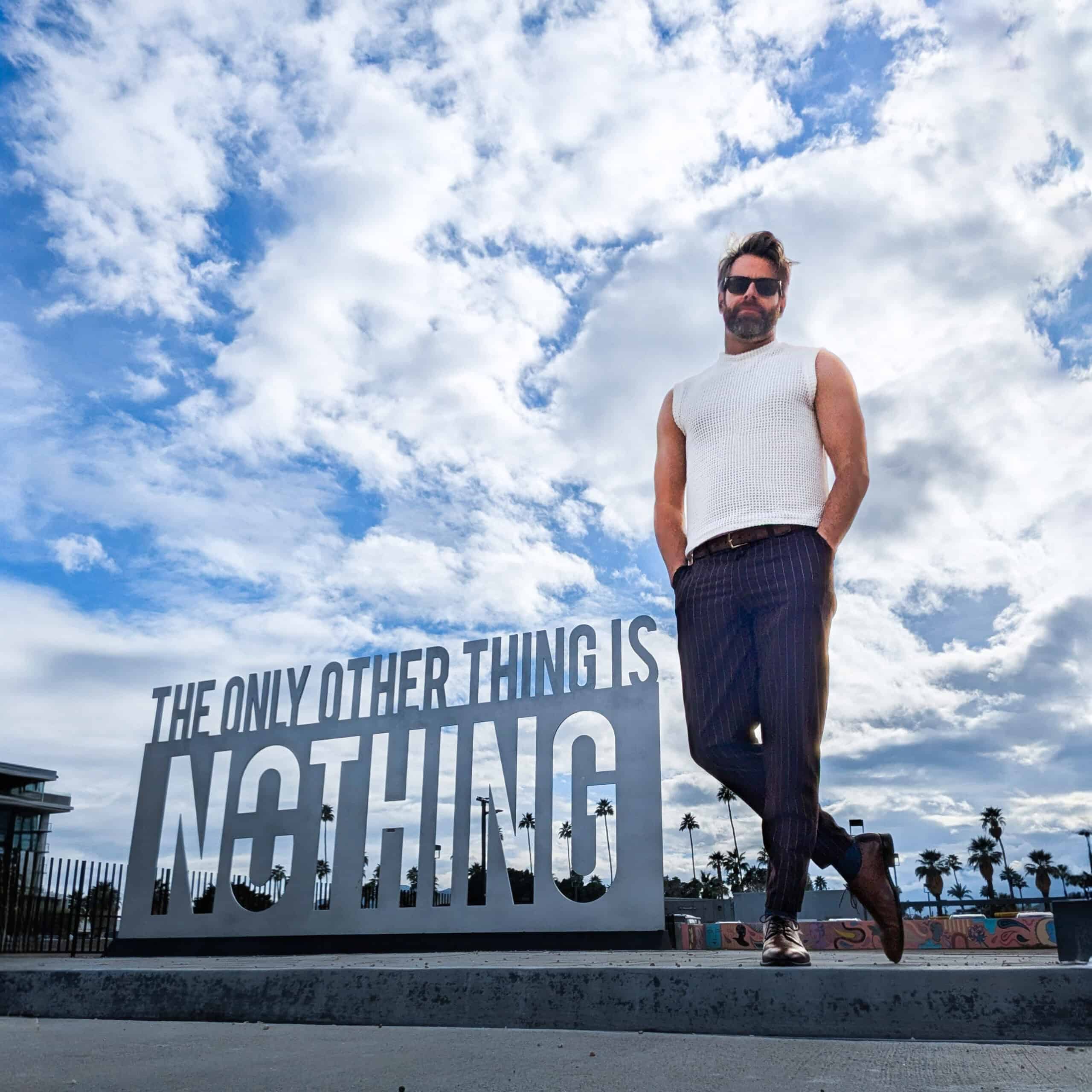 Man standing confidently next to a large sign reading "The only other thing is nothing" under a clou.