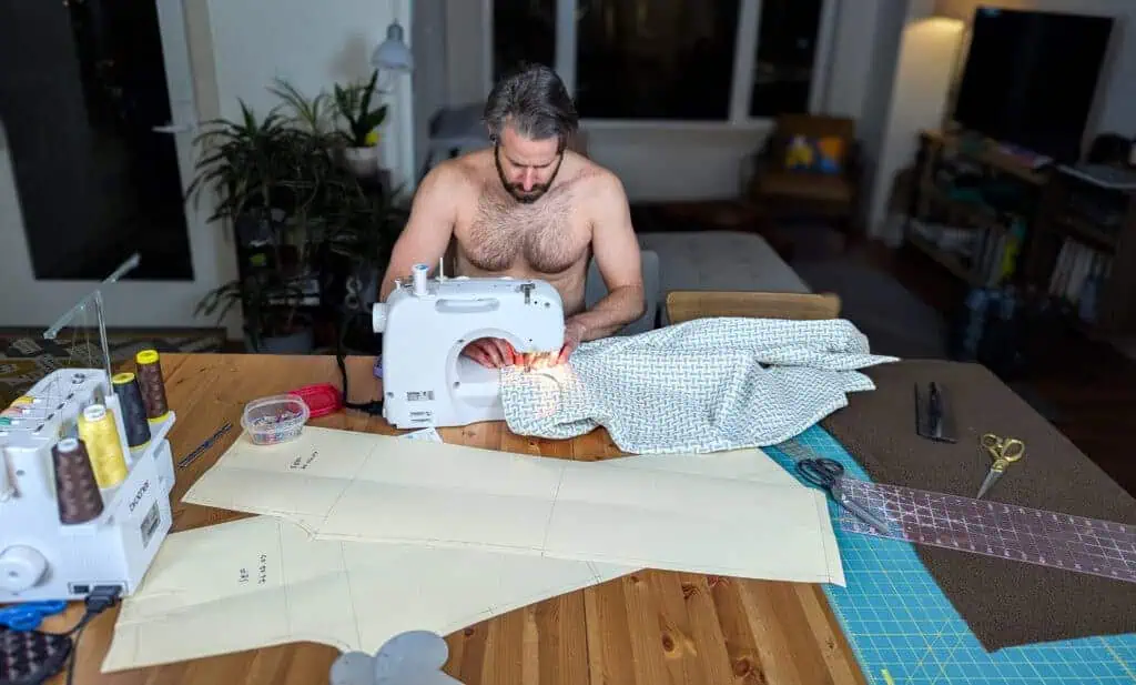 Man shirt sewing with fabric and sewing machine on table.