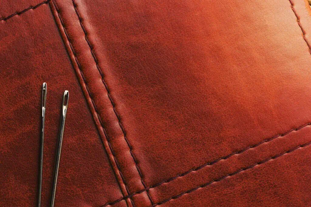 Close-up of a leather garment with visible stitching and a metal pin.
