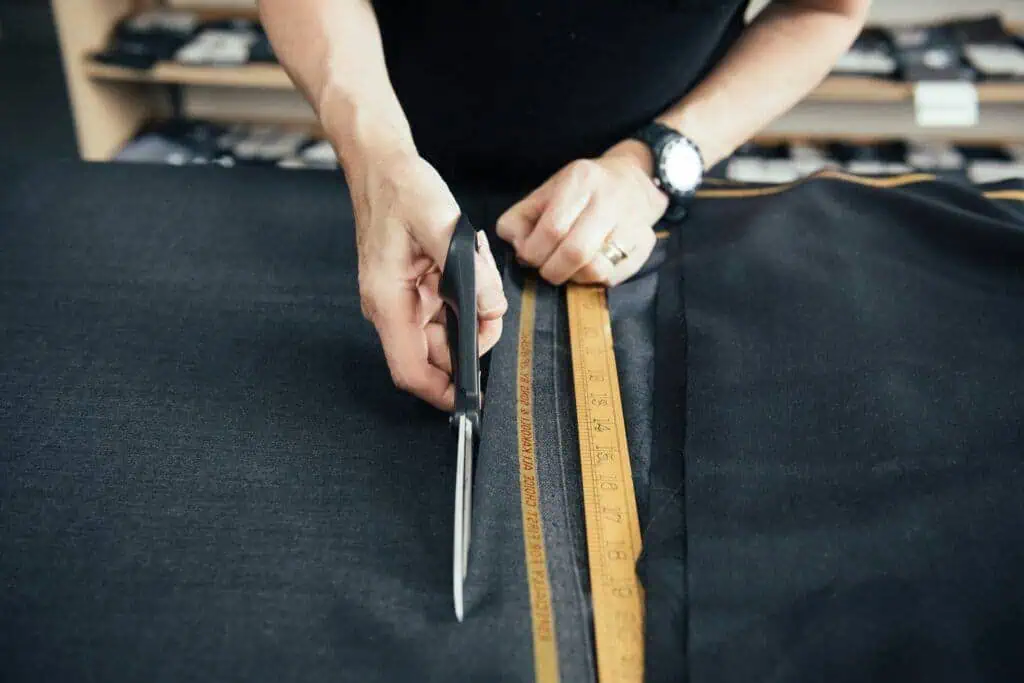 Man cutting fabric with scissors on a suit, measuring with a ruler, in a tailoring studio.
