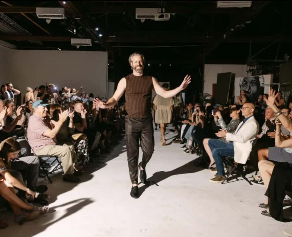 Doug walking on runway wearing sleeveless knit top and dark pants.